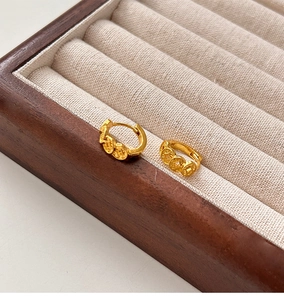Detail of gold-plated coin cluster earrings on a minimalist wooden jewelry display