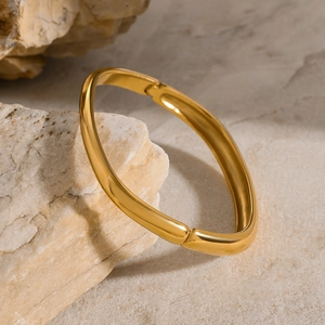 Dettaglio del bracciale quadrato dorato lucido a specchio su sfondo in pietra grezza