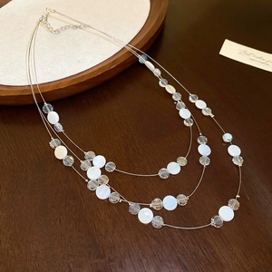 Détail d'un collier multicouche avec des breloques en nacre blanche et cristaux