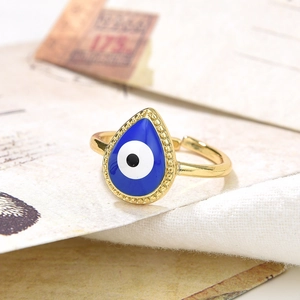 Macro shot of gold adjustable teardrop evil eye ring with blue enamel on beige fabric