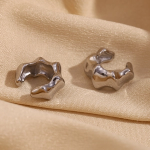 Macro detail of silver fluid metal ear cuffs on elegant champagne silk fabric background
