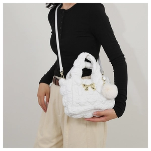 Quilted white cloud crossbody bag featuring a golden bow and soft pompom charm