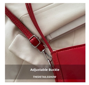 Detail of red patent leather crescent bag featuring adjustable strap and silver metal buckle