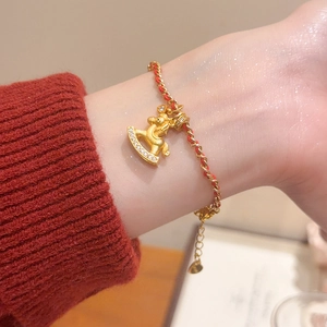 Détail du bracelet cheval à bascule plaqué or 24K avec corde rouge au poignet