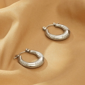 Detailed close-up of silver U-shaped hoop earrings with diamond-cut texture on silk