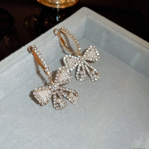 Macro shot of gold bow-shaped earrings with micro-inlaid diamonds and white pearls in a box