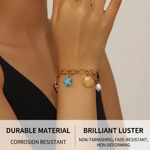 Detail of 18K gold plated bracelet featuring starfish, shell, and pearl charms on wrist