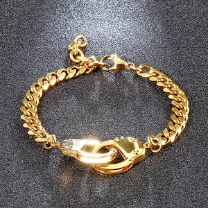 Macro detail of gold handcuff-style stainless steel bracelet on a textured black background