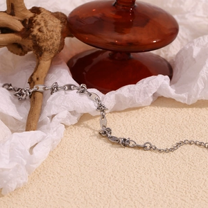 Detail of silver stainless steel coffee bean knot chain bracelet on textured beige display