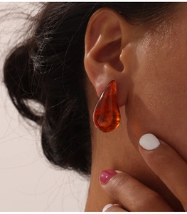 Détail d'une boucle d'oreille goutte en résine ambre portée sur modèle avec effet de lumière