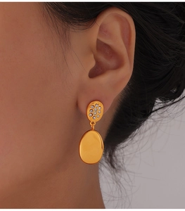 Close-up of golden teardrop drop earrings with zircon crystals on an elegant earlobe