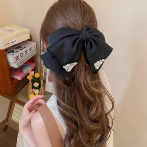 Detailed back view of a large black satin bow hair claw with crystals on long wavy hair