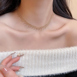 Close-up of a gold woven mesh necklace styled on a model wearing a soft cream sweater