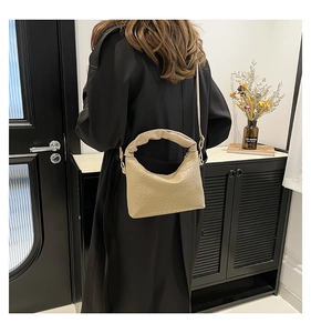 Beige shoulder bag with woven texture and ruched handle styled on a black winter coat
