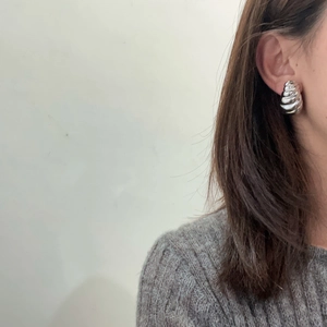 Close-up of geometric twisted silver earring worn on ear with casual grey sweater
