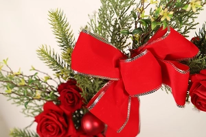 Detailed view of Christmas wreath featuring red velvet bows, roses and evergreen pine branches
