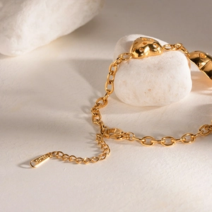 Close-up of golden stainless steel heart bracelet on white pebble with soft shadows