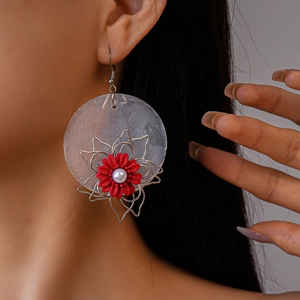 Detail of red flower drop earrings with a pearl center and silver hook on a model