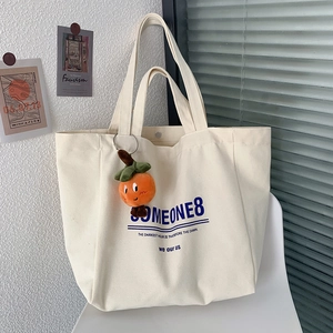 Minimalist canvas tote bag with Someone8 print and orange plush charm on white chair