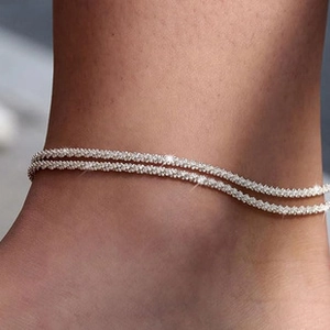 Macro detail of a double-layered silver anklet with sparkling diamonds on a model ankle