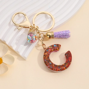 Detail of glitter resin letter C keychain with purple tassel and golden hardware