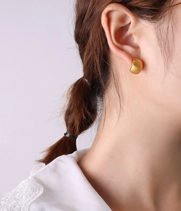 Close-up of matte 18K gold plated C-shaped hoop earrings worn by a model in soft light