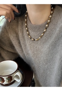 Détail d'un collier de perles en œil de tigre doré porté sur un pull en mohair gris