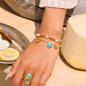 Detail view of gold starfish ring and pearl bracelet on hand with tropical beach props