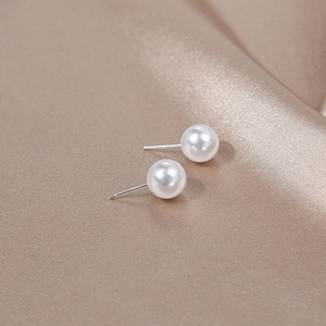 Macro shot of elegant round white pearl earrings on a luxurious silk background