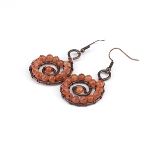 Detail of handmade bronze wire wrapped yoga earrings with orange crystal stones