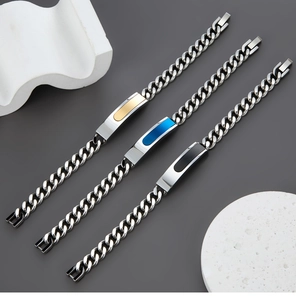 Close-up of Cuban chain bracelets with gold, blue, and black metal plates on stone props