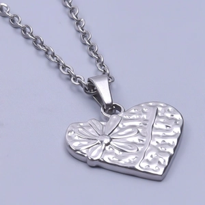 Gros plan du pendentif cœur argenté avec texture florale gravée et chaîne élégante