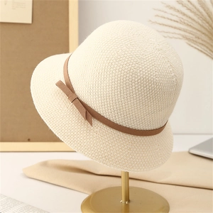 Elegant cream knit cloche bucket hat with brown bow tie on a gold display stand