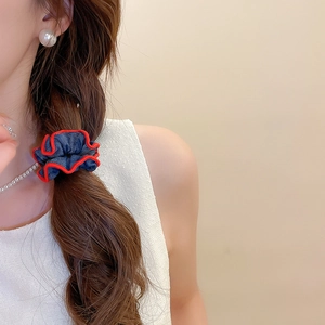 Detailed close-up of blue denim scrunchie with red stitching on a braided hairstyle