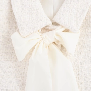 Détail d'une veste en tweed blanc crème avec un grand nœud en soie et texture