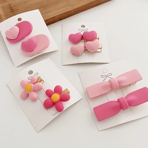 Close-up of matte pink hair clip set featuring heart, flower and bow designs