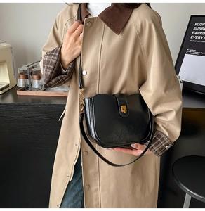 Close-up of black leather saddle bag with golden buckle on a minimalist cafe counter
