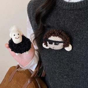 Handmade plush sheep and cartoon character pins on a grey vest and brown suede bag