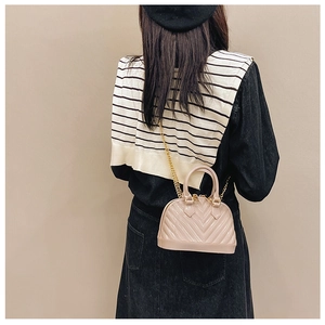 Close-up of quilted nude beige shell bag with chic gold chain strap and textured V-pattern