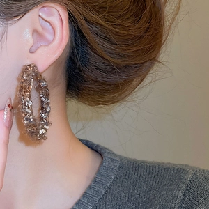 Gros plan de créoles géométriques en tricot marron portées par un mannequin en studio