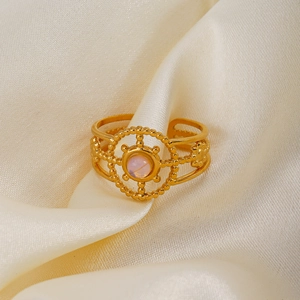 Gold hollow stainless steel ring with pink gemstone on beige silk background