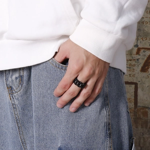 Detail of a black stainless steel watch band style ring worn by a model in a street style look