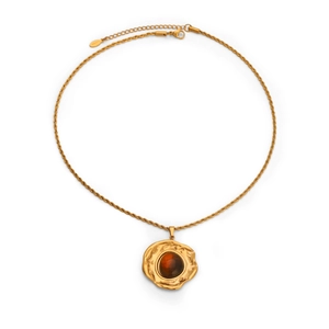 Detailaufnahme einer gehämmerten Goldkette mit einem bernsteinfarbenen Edelsteinanhänger.