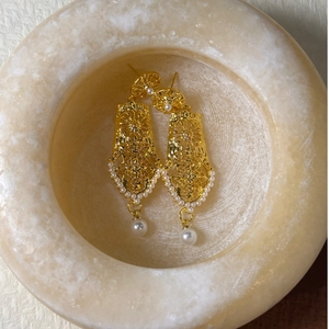 Macro view of gold hollowed metal earrings with elegant white pearl pendant detail