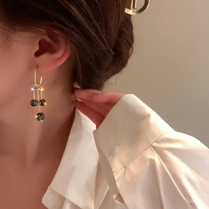 Détail de boucles d'oreilles pampilles dorées avec trois sphères en strass noirs brillants