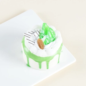 Detailed view of artificial cake model with green glaze and kiwi fruit on ceramic plate