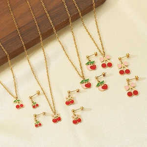 Dettaglio di set gioielli con ciliegie rosse e catene dorate su sfondo di beige