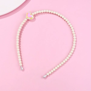 Detail of white pearl headband featuring a pink heart charm on a soft pink background