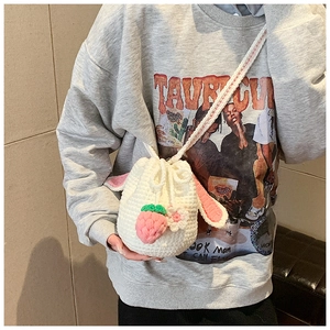 Close-up of handmade crochet bucket bag featuring pink bunny ears and strawberry charms