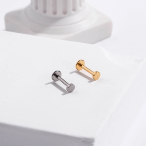 Close-up of gold and silver G23 titanium flat back push-pin studs on stone pedestal